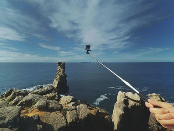 Cropped image of hand holding monopod against sea