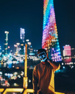 Rear view of man standing against illuminated city at night