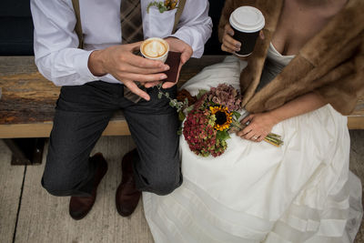 High angle view of newlywed couple holding coffee cups while sitting on bench