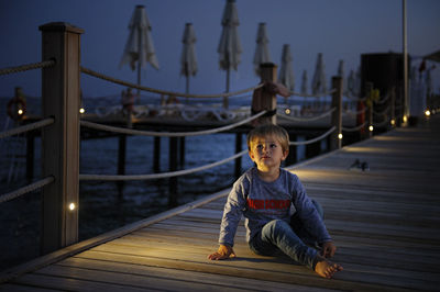 Full length of boy sitting by sea on pier at night