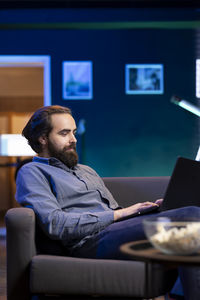 Side view of man using mobile phone while sitting at home