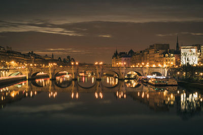 Illuminated pont neuf over seine river amidst buildings against sky at night