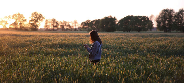 Panoramic view of woman using phone on grassy field during sunset