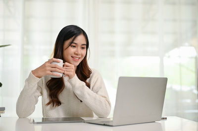 Young woman using mobile phone while sitting on table