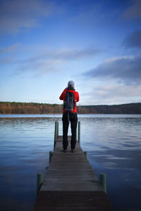 Rear view of man standing on pier over lake against sky
