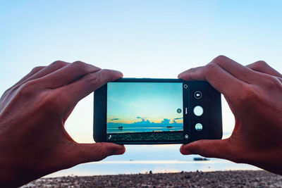 Midsection of person photographing with mobile phone against sky