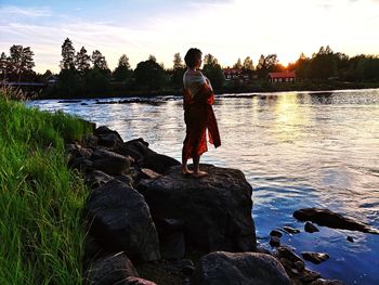 Rear view of man standing on rock by lake against sky