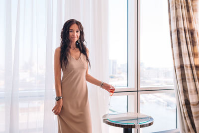 Portrait of smiling young woman standing against window