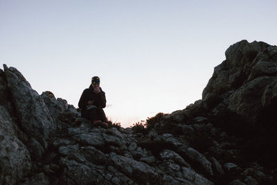 Man sitting on rock against clear sky