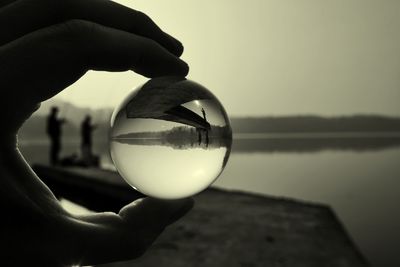 Close-up of hand holding ball with reflection against sky