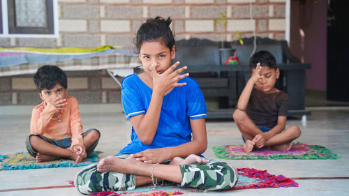Three indian little kids doing meditate yoga asana on roll mat at home.