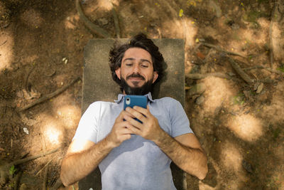  man using smartphone at day time lying down on a bench at a park. mobile phone, technology, nature 