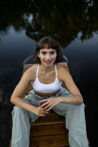 Portrait of young woman sitting by lake