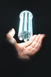 Close-up of hand holding light bulb against black background