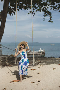 Full length of woman sitting on swing at beach against sky