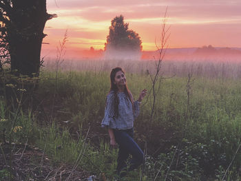 Portrait of young woman standing on field against sky during sunset