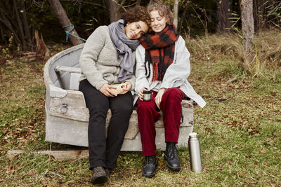 Young female couple sitting on old boat and drinking hot drinks