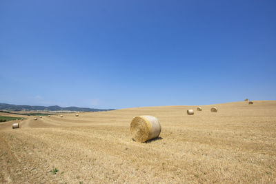 Hay bales on field against clear blue sky