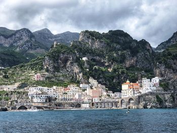 Town by sea and mountains against cloudy sky