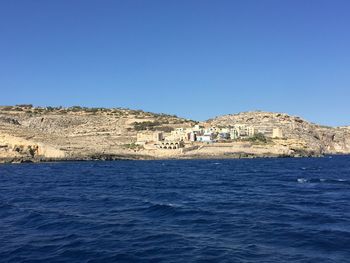 Scenic view of sea by buildings against clear blue sky