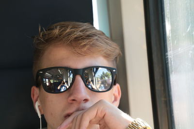 Close-up of man wearing sunglasses with reflection of friend photographing while traveling in train