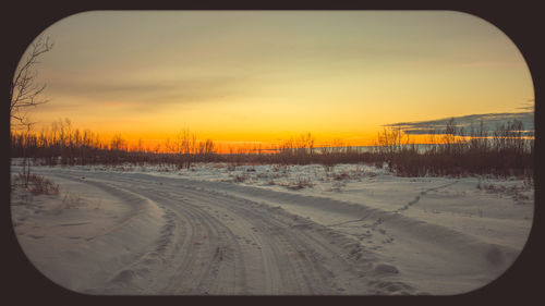 Snow covered landscape against sky during sunset