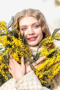 Portrait of a young woman with blond hair holding a bouquet of mimosa in her hands. spring.
