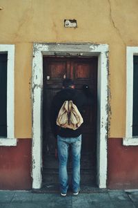 Rear view of man standing against door of building