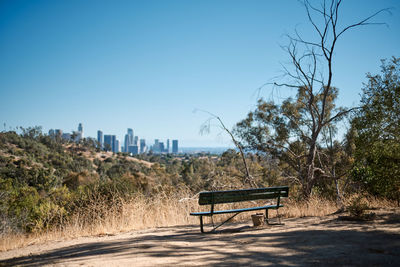 Empty bench on field against clear blue sky