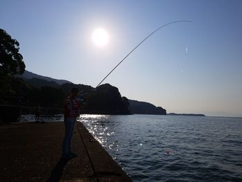 Man fishing in sea against sky