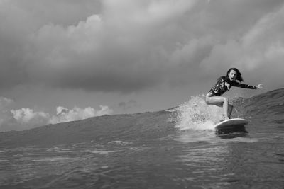 Woman with funny face surfing in the sea against sky