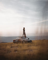 Woman standing on motorcycle on field against sky