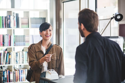 Businesswoman smiling while receiving card to male entrepreneur at counter in office