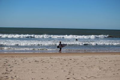 Side view of a surfer walking on calm beach