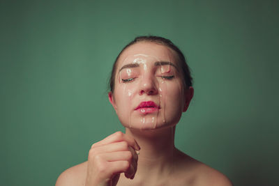 Close-up of woman with water on face against green background