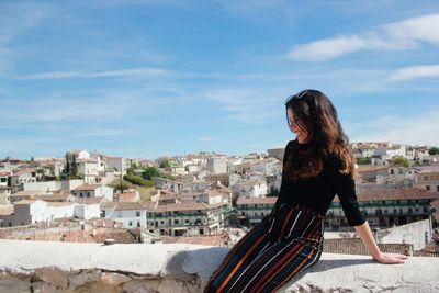 Woman sitting on retaining wall against sky