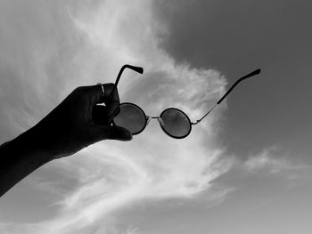Low angle view of hand holding sunglasses against sky