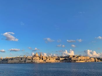 Buildings by sea against blue sky