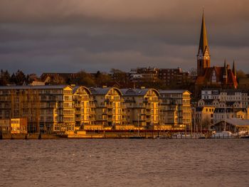 View of buildings at waterfront against cloudy sky