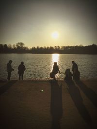 Rear view of silhouette men on lake against sky during sunset