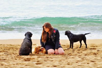 Woman with dog sitting on beach against sky