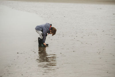 Full length view of cute boy on beach examining a stone