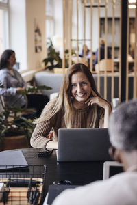 Portrait of smiling businesswoman sitting with laptop at desk in office