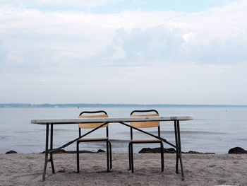 Chairs and table at beach against sky