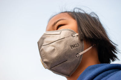 Close-up of girl wearing pollution mask against sky