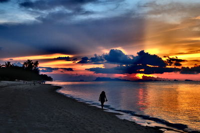 Silhouette person walking on beach against sky during sunset