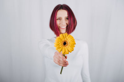 Studio portrait millennial woman with bright red color hair and yellow flower.