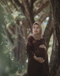 Woman standing by tree trunk in forest