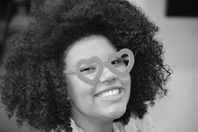 Close-up portrait of smiling woman with curly hair wearing novelty glasses at home