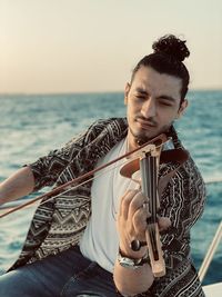 Portrait of young man  playing guitar against sea during sunset